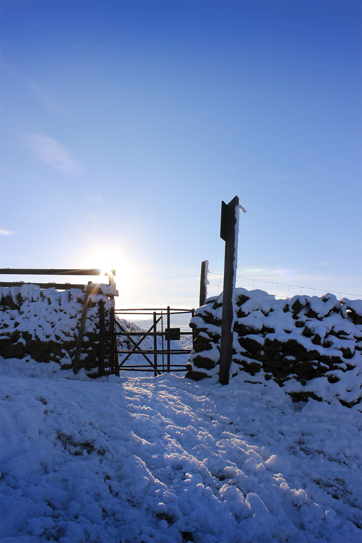 Sun Kissing Gate - Photo of the sun glinting over a snowy kissing gate in Hayfield in the Peak District - photo by gavstretchy